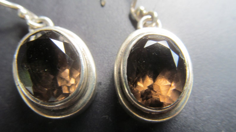 May include: A pair of silver earrings with oval-shaped smoky quartz gemstones. The earrings have a simple design with a smooth silver setting.