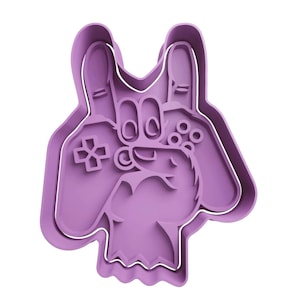 May include: A light purple cookie cutter shaped like a hand making a rock and roll gesture while holding a video game controller. The design features raised interior edges that define the fingers, the controller buttons, and the D-pad.