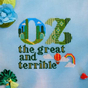 May include: A blue cross-stitch embroidery with the text "Oz the great and terrible" and a depiction of the letter "Oz" with a green and yellow color scheme.