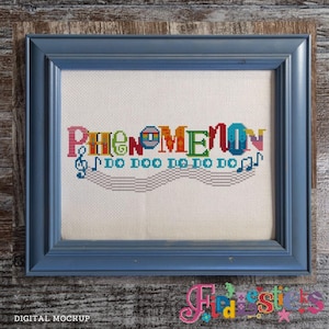 May include: A blue framed cross-stitch with the word "Phenomenon" in colourful letters and musical notes. The cross-stitch is on white fabric and is a digital mockup.