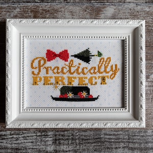 Puede incluir: Bordado a punto de cruz enmarcado en blanco con un lazo rojo, un paraguas verde y un sombrero negro con flores. El texto dice "Practically PERFECT".