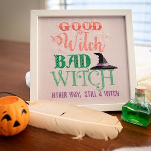 May include: A white framed cross-stitch with the text "Good Witch Bad Witch Either Way, Still a Witch". The cross-stitch features a green witch hat with a purple band.
