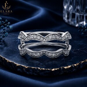 May include: A silver-toned double-band ring featuring a wavy, chevron-inspired silhouette. Both bands are adorned with small, clear, round-cut stones set along the top edges, accented by delicate milgrain detailing along the metal borders.