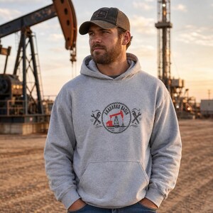 May include: A light gray hooded sweatshirt featuring a circular graphic on the chest. The graphic displays a red oil pump jack, the text "ANADARKO BASIN," and crossed wrenches on either side. The hoodie has long sleeves and a front kangaroo pocket.
