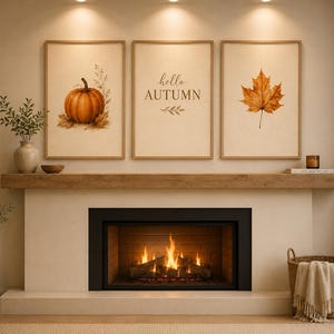 May include: Three framed wall art prints displayed above a fireplace. The left print features an orange pumpkin, the center print contains the text "hello AUTUMN" with leaf accents, and the right print shows a single brown maple leaf.