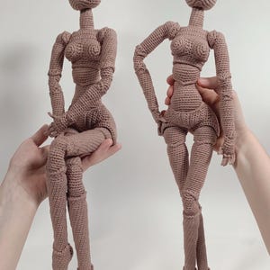 Peut inclure: Deux poupées au crochet marron clair avec des articulations, des têtes arrondies et des membres définis. Les poupées présentent une construction en fil texturé et sont posées debout et assises. Le texte MASTERBLOOM est visible en bas.