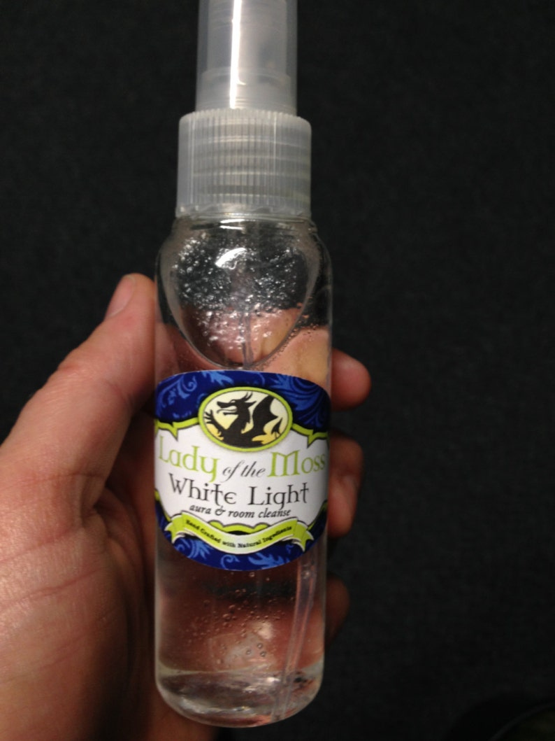 Pode incluir: Uma garrafa de vidro transparente com um bico de pulveriza&ccedil;&atilde;o branco e um r&oacute;tulo que diz "Lady of the Moss White Light aura & room cleanse". O r&oacute;tulo apresenta um design de drag&atilde;o verde e azul.