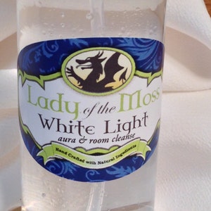 Pode incluir: Uma garrafa de vidro transparente com um r&oacute;tulo azul e verde que diz "Lady of the Moss White Light aura & room cleanse Hand Crafted with Natural Ingredients". O r&oacute;tulo apresenta um drag&atilde;o verde sobre um fundo amarelo.