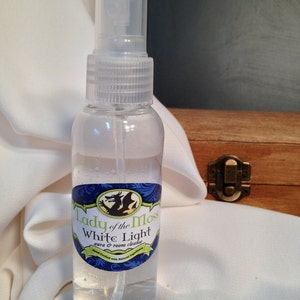 Pode incluir: Uma garrafa de vidro transparente com um bico de pulveriza&ccedil;&atilde;o e um r&oacute;tulo azul e verde que diz "Lady of the Moss White Light aura & room cleanser". Feito &agrave; m&atilde;o com ingredientes naturais.