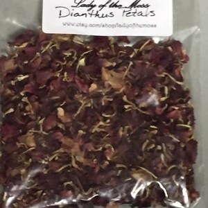 May include: A clear plastic bag filled with dried red and brown Dianthus petals. The bag has a white label with the text "Lady of the Moss Dianthus Petals" and a website address.