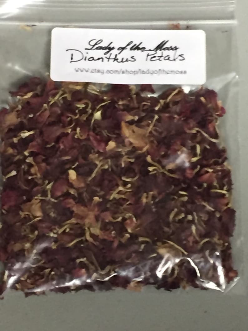 May include: A clear plastic bag filled with dried red and brown Dianthus petals. The bag has a white label with the text "Lady of the Moss Dianthus Petals" and a website address.