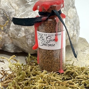 May include: A small glass bottle with a red wax seal and a black ribbon tied around the neck. The bottle contains a brown powder and has a label that reads "Lady of the Moss Be Gone Incense".