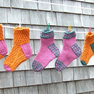 Könnte beinhalten: Sechs Paar Stricksocken hängen an einer Wäscheleine. Die Socken sind in verschiedenen Farben, darunter Orange, Pink und Grün.