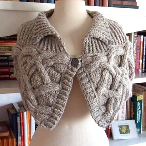 May include: A gray knitted shawl with a cable knit pattern and a collar. The shawl has two buttons on the front.