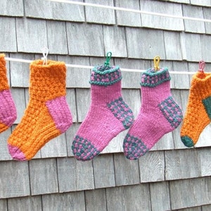 Pode incluir: Seis pares de meias de tricô pendurados em um varal. As meias são de várias cores, incluindo laranja, rosa e verde.