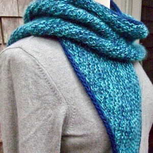 May include: A teal and blue knitted scarf with a dark blue border. The scarf is folded and draped over a mannequin's neck.