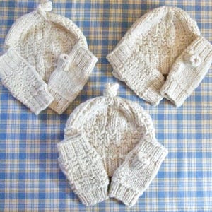 May include: Three sets of knitted hats and fingerless gloves in a cream color. The hats have a textured knit pattern and the gloves have a simple knit pattern.