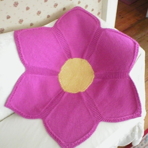 May include: A pink knitted flower blanket with a yellow center. The blanket is made of soft yarn and has a delicate, feminine design.