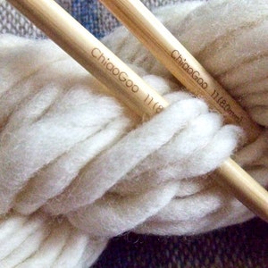 May include: Two wooden knitting needles with the brand name "ChiaoGoo" and the size "11 (8.0mm)" printed on them. The needles are wrapped in a ball of white yarn.