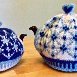 Peut inclure: Deux chauffe-théières en tricot dans un motif géométrique bleu et blanc. Les chauffe-théières sont faites avec un fond blanc et des formes de diamants bleus et bleu clair.