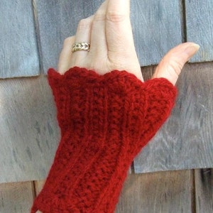 May include: Red knitted fingerless gloves with a scalloped edge. The gloves are made with a textured stitch pattern.