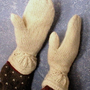 May include: A pair of knitted mittens in a cream color with a brown and white patterned cuff. The mittens have a simple design with a textured knit.