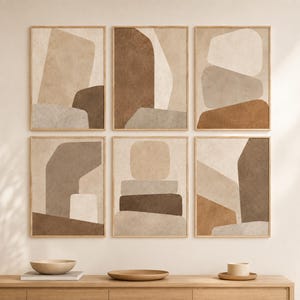 May include: A set of six framed wall art prints arranged in two rows of three. Each print features abstract geometric shapes in a neutral colour palette of beige, tan, taupe, and dark brown with a textured, matte finish and light wood frames.