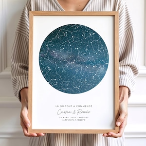 Könnte beinhalten: Ein gerahmter Druck mit einer Himmelskarte in einem kreisförmigen Design. Das Kunstwerk zeigt einen dunkelblauen Hintergrund mit weißen Sternbildern. Der Text "LÀ OÙ TOUT A COMMENCÉ Cassia & Roméo 24 AVRIL 2024 ANTIBES 43.581286°N, 7.124207°E" ist darunter. Der Rahmen ist aus hellem Holz.