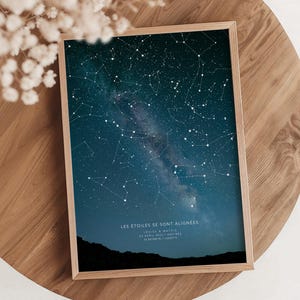 May include: A framed print featuring a dark blue night sky filled with white stars and constellations. The print includes the text "LES ÉTOILES SE SONT ALIGNÉES" and additional details. The frame is made of light-colored wood.