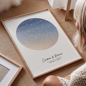 Könnte beinhalten: Gerahmter Druck mit einer Himmelskarte in einem blau-beigen Farbverlaufskreis. Der Druck enthält die Namen "Cassia & Roméo" sowie Datum und Ort. Der Rahmen ist aus hellem Holz.