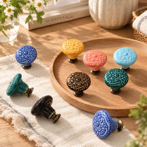 May include: A collection of nine ceramic cabinet knobs in various colors including yellow, pink, light blue, dark blue, teal, black, and brown. Each knob features a raised floral pattern on the circular face and a metallic base.