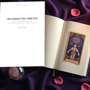 K&ouml;nnte beinhalten: Ein wei&szlig;es Buch mit dem Titel UNLOCKING THE THIRD EYE Companion Workbook & Journal von Jessie C. Ewing III, neben einem offenen Tagebuch mit einer Tarotkarte, die eine Figur unter einer Sonne zeigt, einem goldenen Stift und zwei brennenden Kerzen auf violettem Stoff.