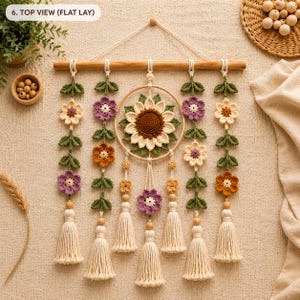 May include: A wall hanging featuring a central crochet sunflower inside a wooden hoop, surrounded by four vertical strands of crocheted flowers in purple, orange, and cream with green leaves, finished with cream-colored yarn tassels.