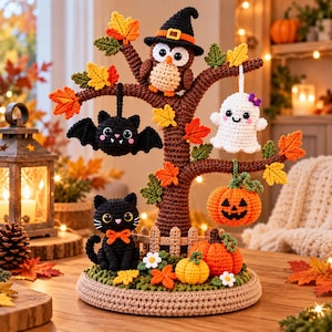 Puede incluir: Un adorno de Halloween tejido a ganchillo que muestra un árbol marrón con hojas naranjas, amarillas y verdes. Los adornos colgantes incluyen un murciélago negro, un fantasma blanco y una calabaza naranja. Un gato negro y dos calabazas están en la base.