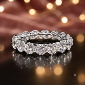 Op de afbeelding: Een zilverkleurige eternity-ring met een doorlopende rij ronde, heldere stenen gezet in een gepolijst metalen montuur. De ring heeft een hoogglans afwerking met meerdere facetten die het licht vangen, wat zorgt voor een schitterende glans over de gehele omtrek van de cirkelvormige band.