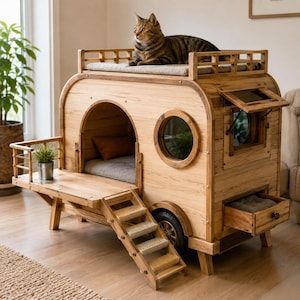 May include: A wooden cat house shaped like a vintage camper trailer, featuring a roof deck with a cushion, a front porch with stairs, a circular window, a side awning window, and a small storage drawer. A tabby cat rests on the roof.
