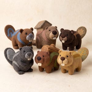 May include: A collection of six needle-felted beaver figurines in various colors including brown, gray, and tan. Each beaver features small black eyes, prominent white teeth, and a unique tail design, such as a leaf, tree, or geometric pattern.
