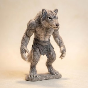 May include: A needle-felted werewolf figurine in shades of grey, standing on a textured base. The creature features a muscular build, pointed ears, and a dark grey loincloth. Its fur has a coarse, fibrous texture, and it is posed in a standing position.