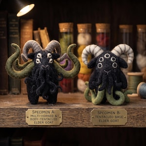 May include: Two needle-felted goat figurines with multiple eyes and horns. The left figure is labeled 'SPECIMEN A: MULTI-HORNED & BODY-TENTACLED ELDER GOAT' and the right is labeled 'SPECIMEN B: TENTACLED BASE ELDER GOAT'. Both feature dark wool.