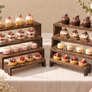 May include: Two sets of four-tiered dark brown wooden display risers arranged in a staircase pattern. Each level holds various desserts including cupcakes, small parfaits, macarons, and fruit tarts, showcasing a rustic wood grain texture.