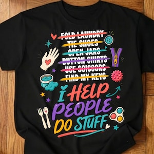 May include: A black t-shirt featuring a graphic with the text FOLD LAUNDRY, TIE SHOES, OPEN JARS, BUTTON SHIRTS, USE SCISSORS, FIND MY KEYS, and I HELP PEOPLE DO STUFF. The design includes colourful illustrations of a hand, zipper, button, and sensory toys.