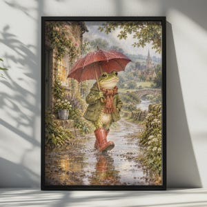 Puede incluir: Una lámina de arte enmarcada que representa una rana con chaqueta verde, bufanda marrón y botas de agua rojas mientras sostiene un paraguas rojo. La rana camina por un charco en un camino de piedra en un pueblo lluvioso con un puente.
