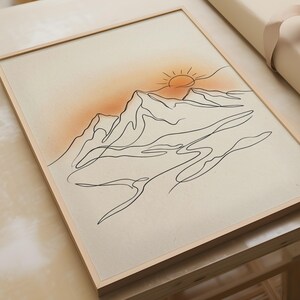 Pode incluir: Uma impressão de arte emoldurada apresentando um desenho de linha preta contínua de picos de montanhas e um sol. O fundo é de cor creme claro com um brilho laranja suave e degradê atrás do sol, tudo em uma moldura de madeira de tom claro.