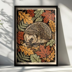 May include: A framed print featuring a central hedgehog illustration surrounded by a dense pattern of autumn leaves in shades of red, orange, yellow, and sage green against a dark background, enclosed in a simple black frame.
