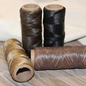 May include: Four spools of waxed thread in shades of tan, dark brown, black, and medium brown. Each spool features a cardboard core and a textured, braided appearance, arranged with two spools standing upright and two spools lying horizontally.