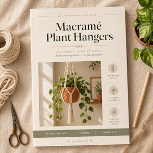 Peut inclure: Un livre d'instructions à couverture souple intitulé Macramé Plant Hangers: A Fiber & Fringe Field Guide. La couverture présente une photographie d'une plante en pot dans une suspension en macramé crème, avec des détails sur cinq nœuds et trois projets.