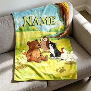 May include: A soft fleece blanket featuring a colorful illustration of a duck, a brown bear, an owl, a black and white cat, and a chicken in a grassy field. The word NAME is printed in large yellow letters at the top under a blue sky.