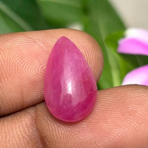 May include: A teardrop-shaped gemstone with a smooth, polished surface and a vibrant, deep pink color. The stone features a translucent quality that catches the light, showcasing its rounded edges and symmetrical form in a clear, focused view.