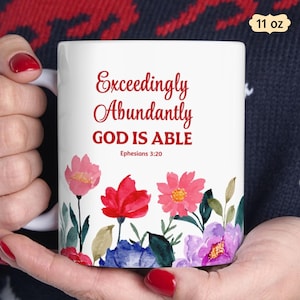 May include: A white 11 oz ceramic mug featuring red text that reads Exceedingly Abundantly GOD IS ABLE Ephesians 3:20. The base of the mug is decorated with a colorful watercolor floral pattern including pink, red, blue, and purple flowers.