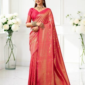 May include: A vibrant pink saree featuring intricate gold metallic woven patterns throughout the fabric. The garment includes a matching short-sleeved blouse with a V-neckline, draped elegantly to showcase the detailed gold border and motifs.